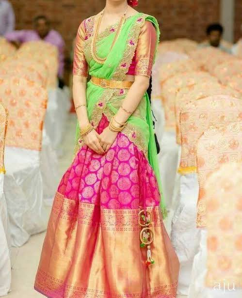 Half saree in bright pink zari-butta silk with a wide gold border, worn with a contrasting parrot-green blouse, green dupatta and gold waist belt.